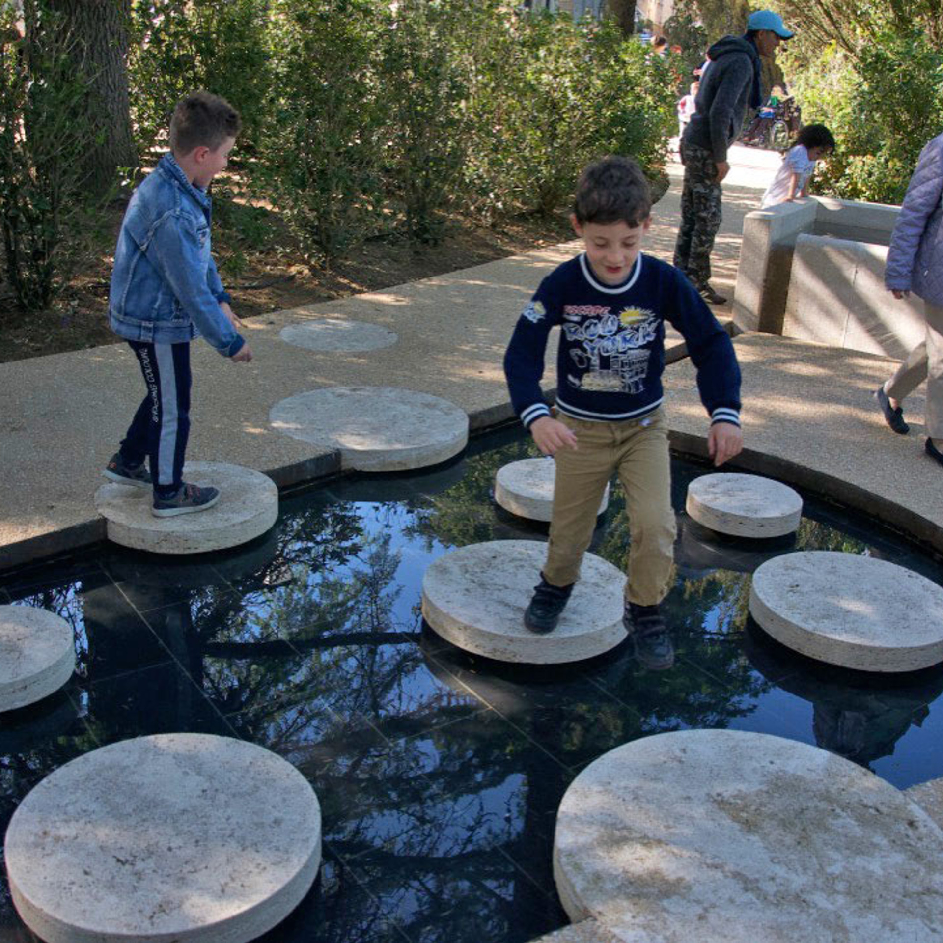 Children playing on travertine stepping stones in water feature